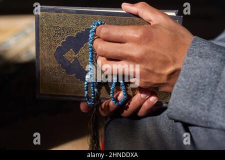 Nahaufnahme der Hände eines muslimischen Mannes, der islamische Gebetsperlen und den Koran hält Stockfoto