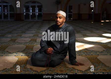 Offene Aufnahme eines muslimischen Mannes, der in einer Moschee auf dem Boden sitzt Stockfoto