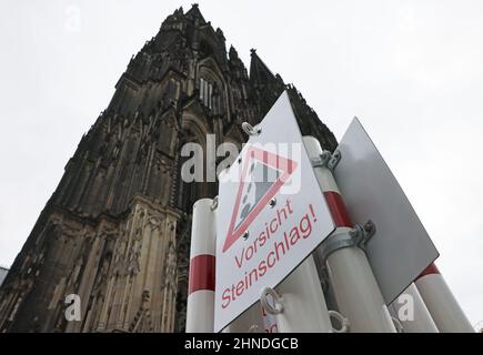 Köln, Deutschland. 16th. Februar 2022. Auf der Domplatte sind Warnschilder auf einer Schranke mit der Aufschrift 'Sicht Steinschlag' angebracht, um vor Stürmen aus dem Dom fallenden Steinen zu warnen. Zwei Hurrikan-Tiefstände in schneller Folge verursachen in vielen Teilen Deutschlands Unwetterwarnungen. Quelle: Oliver Berg/dpa/Alamy Live News Stockfoto