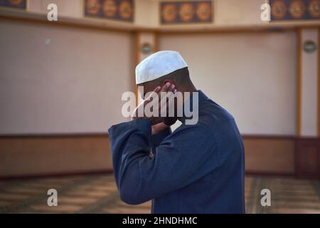 Ein junger Muslim betet in einer Moschee, wobei seine Hände bis zu seinen Ohrläppchen angehoben sind Stockfoto