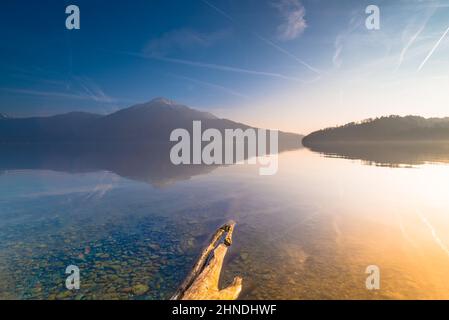 Strahlender Sonnenuntergang über dem See. Der Rigi-Gipfel spiegelt sich im Wasser des Zugersees wider. Kieselsteine und der Strahl im Wasser im Vordergrund. Stockfoto