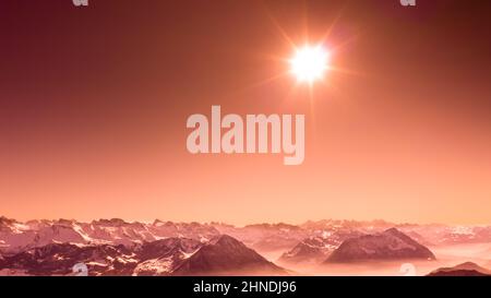 Silhouetten der Berggipfel. Helle Strahlen der Sonne am Himmel. Schweizer Alpen. Rot. Stockfoto