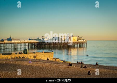 13. Januar 2022: Brighton, East Sussex, Großbritannien - Menschen, die an einem klaren Winterabend am Brighton Beach bei Sonnenuntergang sitzen, in der Nähe der Doughnut Groyne und... Stockfoto