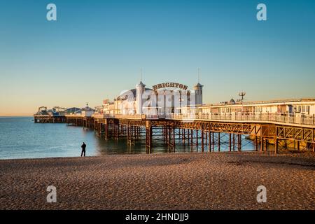 14. Januar 2022: Brighton, East Sussex, Großbritannien - Sonnenaufgang am Brighton Palace Pier, mit einem Mann, der am Strand steht und aufs Meer blickt. Stockfoto