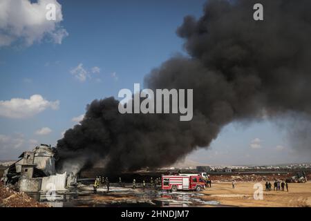 Dana, Syrien. 16th. Februar 2022. Starker Rauch steigt auf, als Mitglieder der syrischen Zivilverteidigung, bekannt als Weißhelme, ein Feuer auslösten, das in einem Treibstofflager ausbrach, als Folge eines Raketenangriffs des syrischen Regimes und russischer Streitkräfte auf das Dorf Tarminin in der Nähe der Stadt Dana. Nach Angaben der Weißhelme wurden bei einem Artilleriebeschuss auf einem Brennstoffmarkt, der angeblich einer dschihadistischen Gruppe angehört, vier Zivilisten getötet und zwei weitere verletzt. Quelle: Anas Alkharboutli/dpa/Alamy Live News Stockfoto