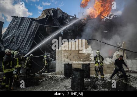 Dana, Syrien. 16th. Februar 2022. Mitglieder der syrischen Zivilverteidigung, bekannt als Weißhelme, arbeiten daran, ein Feuer zu löschen, das in einem Treibstofflager ausbrach, als Folge eines Raketenangriffs des syrischen Regimes und russischer Streitkräfte auf das Dorf Tarminin in der Nähe der Stadt Dana. Nach Angaben der Weißhelme wurden bei einem Artilleriebeschuss auf einem Brennstoffmarkt, der angeblich einer dschihadistischen Gruppe angehört, vier Zivilisten getötet und zwei weitere verletzt. Quelle: Anas Alkharboutli/dpa/Alamy Live News Stockfoto