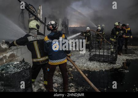 Dana, Syrien. 16th. Februar 2022. Mitglieder der syrischen Zivilverteidigung, bekannt als Weißhelme, arbeiten daran, ein Feuer zu löschen, das in einem Treibstofflager ausbrach, als Folge eines Raketenangriffs des syrischen Regimes und russischer Streitkräfte auf das Dorf Tarminin in der Nähe der Stadt Dana. Nach Angaben der Weißhelme wurden bei einem Artilleriebeschuss auf einem Brennstoffmarkt, der angeblich einer dschihadistischen Gruppe angehört, vier Zivilisten getötet und zwei weitere verletzt. Quelle: Anas Alkharboutli/dpa/Alamy Live News Stockfoto