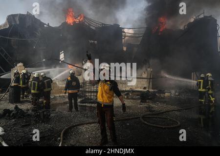 Dana, Syrien. 16th. Februar 2022. Mitglieder der syrischen Zivilverteidigung, bekannt als Weißhelme, arbeiten daran, ein Feuer zu löschen, das in einem Treibstofflager ausbrach, als Folge eines Raketenangriffs des syrischen Regimes und russischer Streitkräfte auf das Dorf Tarminin in der Nähe der Stadt Dana. Nach Angaben der Weißhelme wurden bei einem Artilleriebeschuss auf einem Brennstoffmarkt, der angeblich einer dschihadistischen Gruppe angehört, vier Zivilisten getötet und zwei weitere verletzt. Quelle: Anas Alkharboutli/dpa/Alamy Live News Stockfoto