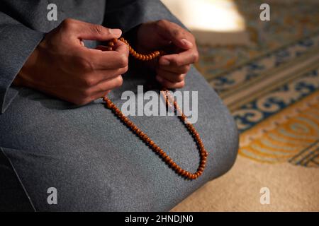 Nahaufnahme der Hände eines muslimischen Mannes, der Gebetsperlen in einer Moschee hält Stockfoto