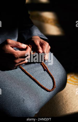 Nahaufnahme der Hände eines muslimischen Mannes, der Gebetsperlen in einer Moschee hält Stockfoto