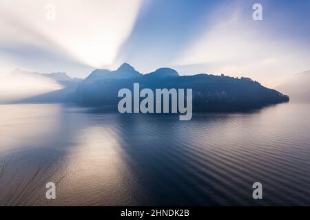 Großartiges Spiel aus Licht und Schatten. Sonnenlicht saß hinter einem Bergrücken. Lichtstrahlen durchdringen den Himmel. Auf dem Wasser des Sees Wellen und Lichtreflexion . Stockfoto