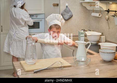 Mutter und Sohn in weißen Chefkleidern schnitten in ihrer eigenen Küche mit einem Messer Birnen. Eine Erwachsene Frau mit einem kleinen Jungen wird einen Kuchen kochen Stockfoto