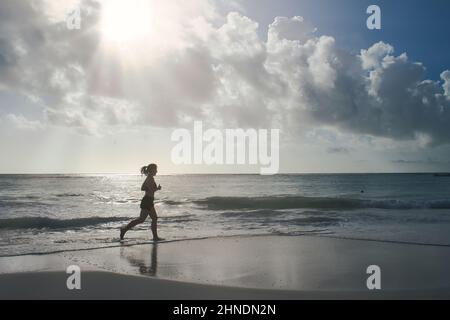 Die junge Sportlerin läuft bei Dawn am tropischen Strand Xpu-Ha in Mexiko Stockfoto