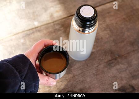 Mittagessen im Freien beim Wandern im Wald - heißer weißer Kaffee in Thermoskanne und hausgemachtes Sandwich auf Holztisch Stockfoto