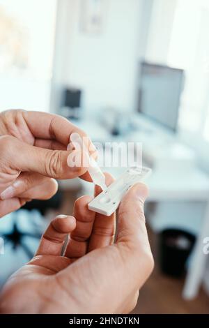 Nahaufnahme eines jungen kaukasischen Mannes im Büro, der seine eigene Probe in das Schnellantigen-Diagnosetestgerät Covid-19 legte Stockfoto