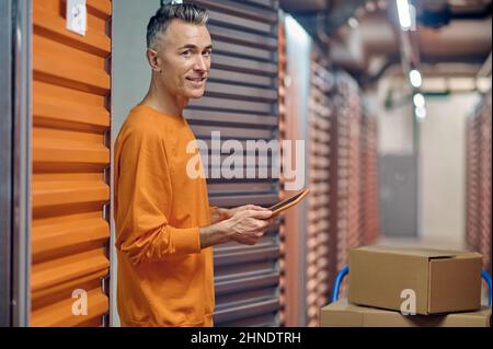 Fröhlicher Lagerangestellter mittleren Alters zwischen Frachtcontainern Stockfoto