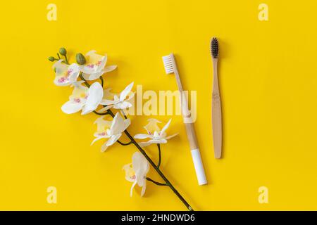 Natürliche umweltfreundliche Bambusbürsten und Orhidblüten auf papiergelbem Hintergrund. Platz für Text oder Ihr Design kopieren Draufsicht Flat Lay. Stockfoto