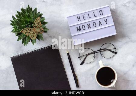 Schreibtisch im Büro oder zu Hause. Lightbox Text Hello monday Schwarzer Notizblock, Tasse Kaffee, Sukulente, Gläser auf Marmorhintergrund Konzept stilvoller Arbeitsplatz Stockfoto