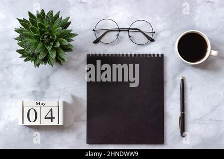 Schreibtisch im Büro oder zu Hause. Holzwürfel Kalender Mai 4th. Schwarzer Notizblock, Tasse Kaffee, Sukulent, Gläser auf Marmorhintergrund Konzept stilvoll arbeitspl Stockfoto