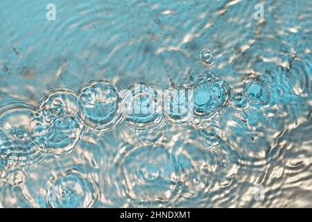Kosmetische Feuchtigkeitscreme mizellares Wasser. Auf der Wasseroberfläche bilden sich Goldpulverpartikel. Abstrakter flüssiger welliger Hintergrund. Stockfoto