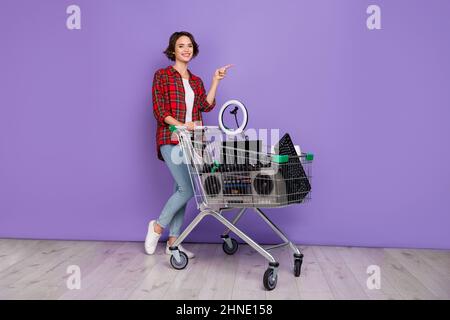 Foto von lustigen jungen Brünette Dame mit Recycling-Artikel in Trolley tragen Hemd Jeans Sneakers isoliert Beton violett Wand Hintergrund Stockfoto