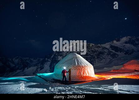 Mann mit geteiltem Snowboard in der Nähe des nomadischen Wohnkomplexes Yurt im Skigebiet Shymbulak in Almaty, Kasachstan. Winternacht Astrofotografie mit Sternen A Stockfoto