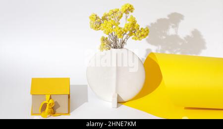 Immerwährende immortelle gelbe Blumen in minimalistischer weißer Keramikvase und gelber Geschenkbox mit Schleife über gelbem und weißem Hintergrund. Greetin Stockfoto