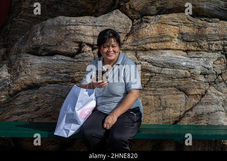 Eine Asiatin mittleren Alters telefoniert vor einem massiven Felsen Stockfoto