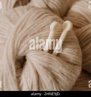 Ästhetisches Bild eines hellen, luftigen, beigen Pastellgarns.Nahaufnahme eines mitteldicken Blasgarns aus Baby-Alpaka und Merinowolle. Stricknadeln stecken in Garnknäuel.Quadratische Ernte für soziale Medien Stockfoto