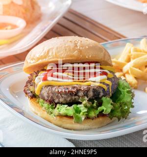 Köstlicher Hamburger mit einem Cutlet auf dem Tisch im Freien Fast Food Lifestyle aus nächster Nähe. Frühstück an der frischen Luft unter der Sonne. Köstliche lun Stockfoto