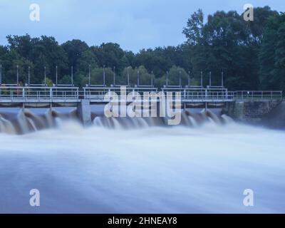 Staumauer am Wasserkraftwerk. Der Wasserabfluss aufgrund der Utensilisierung ist im Gange. Das Wasser fließt durch den Damm in einem breiten und schnellen Strom Stockfoto