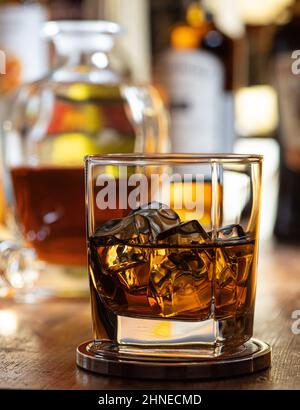 Ein Glas Whisky auf den Felsen auf einer Holzplatte mit Flaschen im Hintergrund Stockfoto