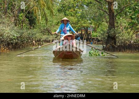 Vietnamesin rudert Touristen entlang des Mekong Flusses in einem traditionellen Holzboot (Sampan), Mekong Delta, Vinh Long Provinz, Südvietnam Stockfoto