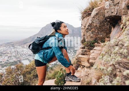 Frau in Sportkleidung, die Schnürsenkel bindet und beim Wandern auf einem Berg aufschaut Stockfoto