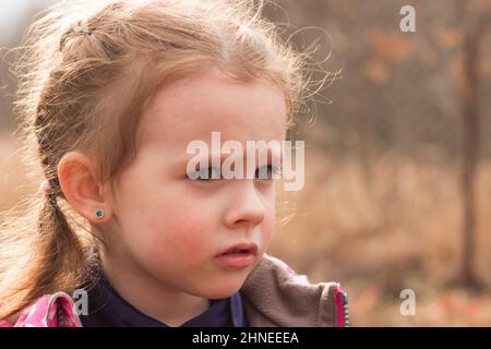 Kleine schöne niedliche traurige Mädchen in einer Jacke mit blonden Haaren in Zöpfen steht auf einem Herbst Hintergrund Stockfoto