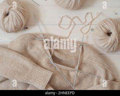 Projekt wird zusammenfügen. Beigefarbener Wollpullover in Strickverfahren Nackenöffnung und Making Hals. Abbildung von oben, um zu veranschaulichen, wie der Pullover mit Stricknadeln am Hals gestrickt wird. Weibliche Hobby Stricken Stockfoto