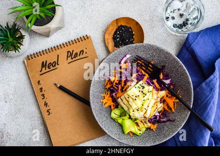 Blick von oben auf eine Schüssel mit Rotkohl, Karotte, grünem Pfeffer und gekochtem Eiersalat und Notizblock mit einer Menüplan-Liste Stockfoto