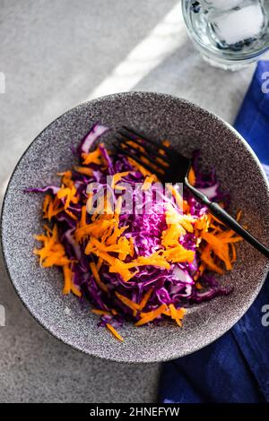 Blick von oben auf eine Schüssel mit geriebenem Karotten- und Rotkohlsalat mit einem Glas Wasser Stockfoto