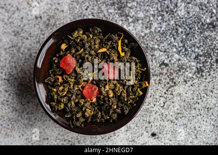 Blick von oben auf eine Schüssel mit grünen sencha-Teeblättern mit getrockneter Mango Stockfoto