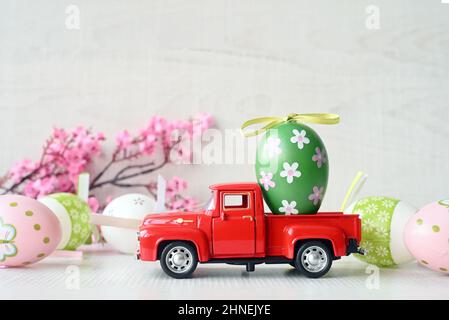 Ein Osterei auf einem kleinen Auto auf grauem Hintergrund und blühender Ast. Speicherplatz kopieren. Osterkarte. Stockfoto