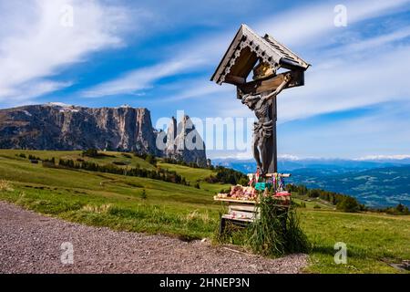 Hügelige Agrarlandschaft mit Weiden und einem Kruzifix bei der Seiser Alm, der Schlerngruppe mit Monte Petz (links) und Santnerspitze (rechts). Stockfoto