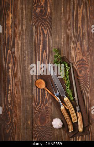 Steakgabel, Messer und Spitzer auf Serviette auf braunem Holzhintergrund Stockfoto