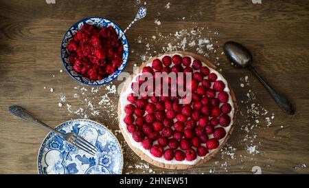 Himbeerkuchen und blaue Porzellanschale gefüllt mit Himbeeren auf einem Holztisch Stockfoto