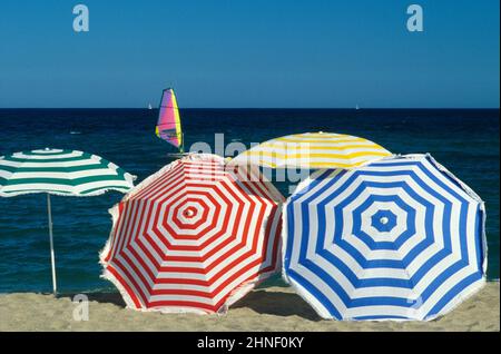 Mehrfarbige Regenschirme mit Strandgraphik, blauem Himmel und Meerwasser, Sommerurlaub Windsurfer Stockfoto