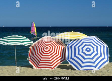 Mehrfarbige Regenschirme mit Strandgraphik, blauem Himmel und Meerwasser, Sommerurlaub Windsurfer Stockfoto