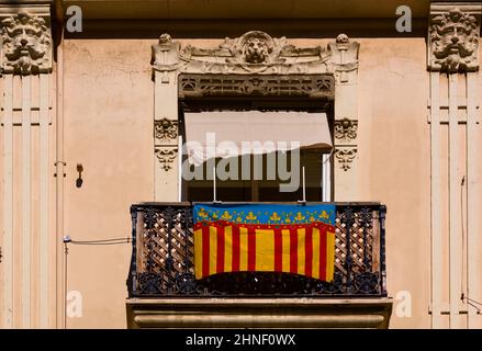 Foto eines Balkons im Zentrum der valencianischen Hauptstadt, von dem eine Flagge der valencianischen Gemeinde hängt Stockfoto