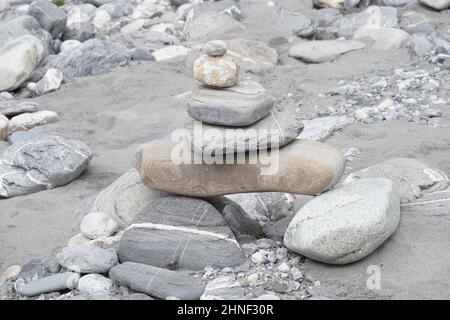 Steinpyramide im Detail. Es liegt an einem sandigen Flussufer mit entkochten Steinen im Hintergrund. Stockfoto