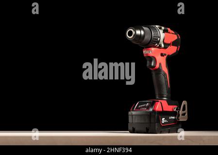 Ein Akkuschrauber steht auf einem Holztisch auf schwarzem Hintergrund. Akku-Bohrmaschine mit Lithium-Ionen-Akku in rot. Professionelles Werkzeug zum Bohren Stockfoto