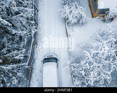 Ein Minivan, der auf einer leeren, schneebedeckten Straße fährt, Luftaufnahme Stockfoto
