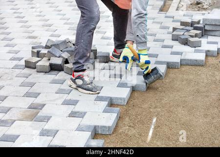 Ein Arbeiter in Handschuhen legt Pflasterplatten mit einem Gummihammer und beobachtet dabei das erforderliche Muster. Stockfoto